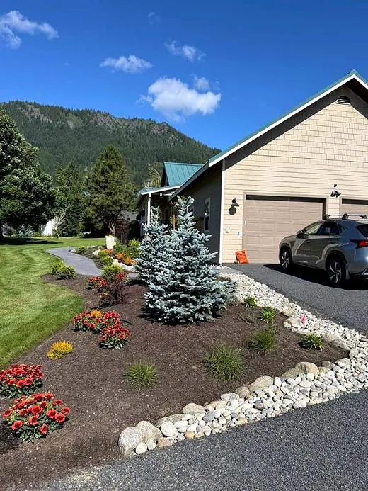 Finished landscape bed near the garage with a blue spruce and river rock border