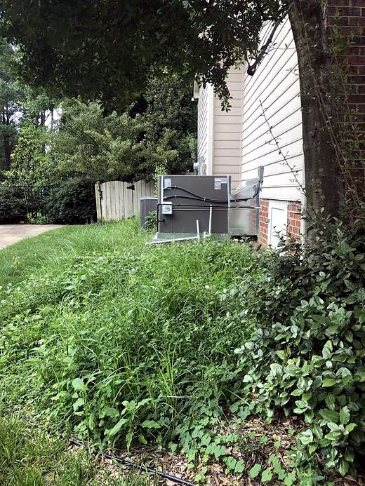 Overgrown grass and weeds around an AC unit before service